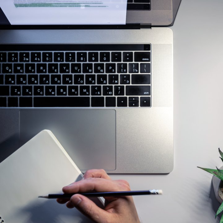 MacBook and a woman’s hand holding a pencil, making notes. Langly logo in the corner.